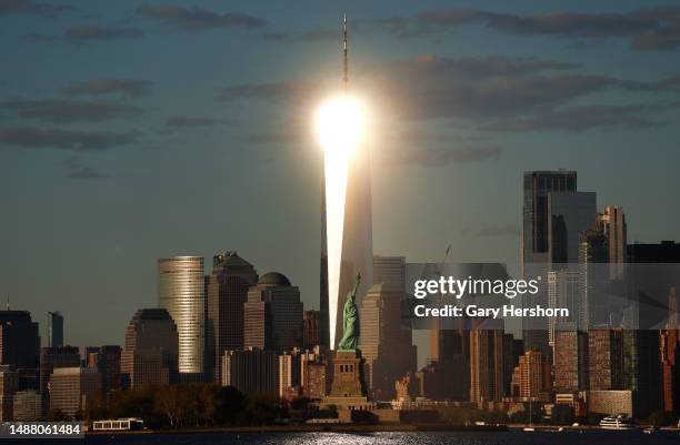 The setting sun reflects off the windows of One World Trade Center behind the Statue of Liberty in New York City on May 6 as seen from Jersey City,...