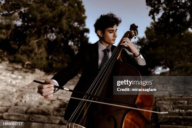 young musician in a black suit plays double bass in the historical arena and in nature. - orchestra outside stock pictures, royalty-free photos & images