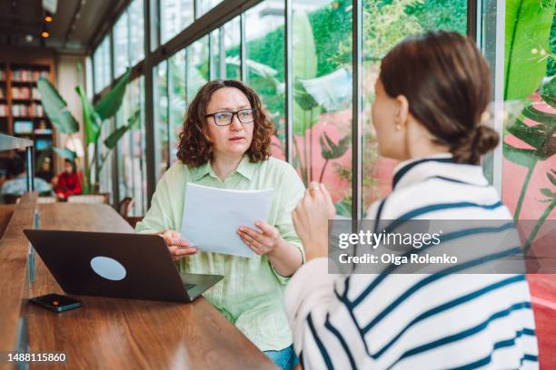 female recruiter with resume paper in hands interviewing and hiring woman candidate for job vacancy in office with glass windows - recruiter stock pictures, royalty-free photos & images