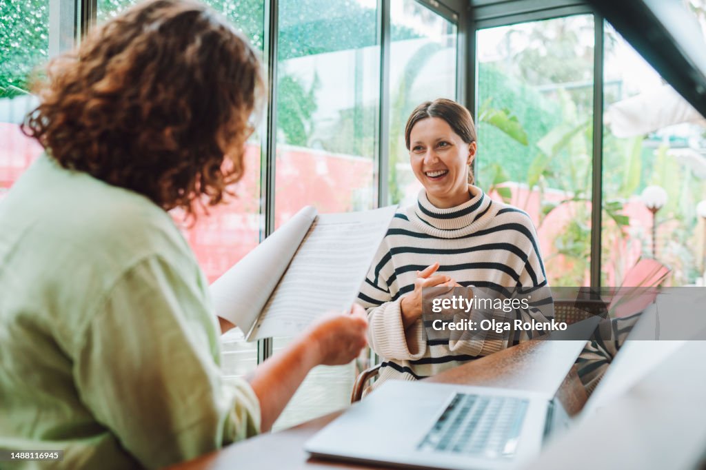 Rearview female recruitment reading and checking resume in hands interviewing and hiring woman candidate for joи near laptop in office with glass windows