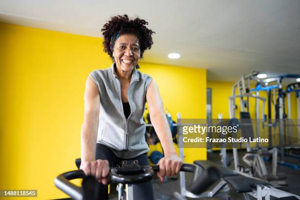 portrait of a senior woman on exercise bike in the gym - black female bodybuilder stock pictures, royalty-free photos & images