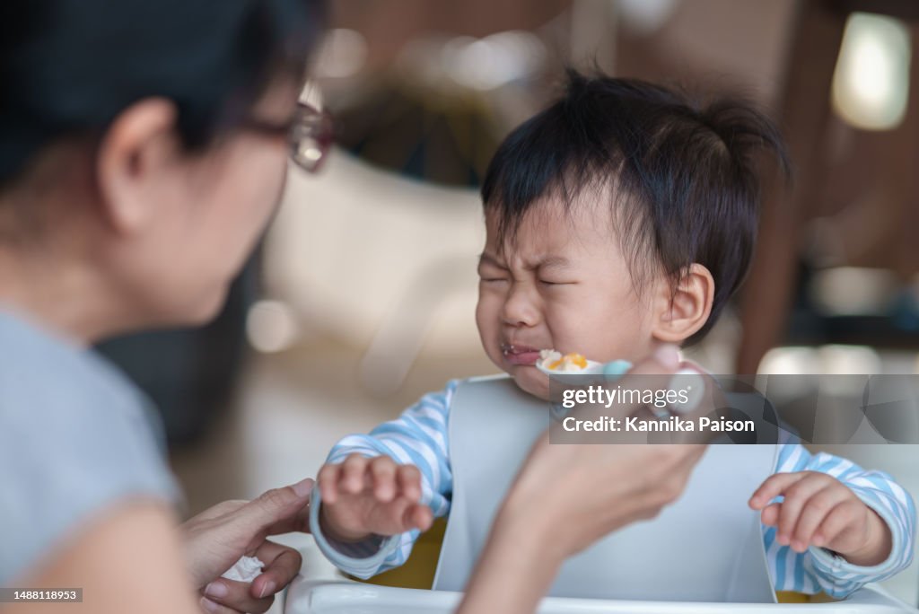 Lindo bebé que se niega a comer y llora mientras su madre lo alimenta.