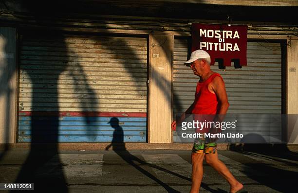 a visitor to giardini naxos taking an early morning stroll past shuttered shops. - giardini naxos stock pictures, royalty-free photos & images