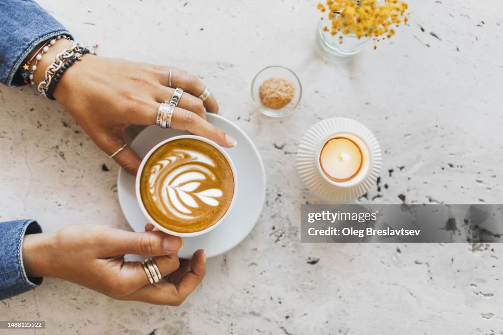 Cup of coffee in female hands. Cup on white textures stone table surface.