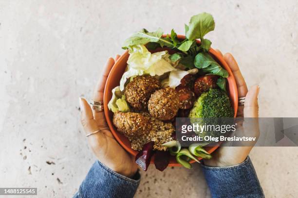 woman's hands holding bowl with falafel, broccoli, greens, cherry tomatoes, red beans, beetroot and quinoa - faláfel fotografías e imágenes de stock