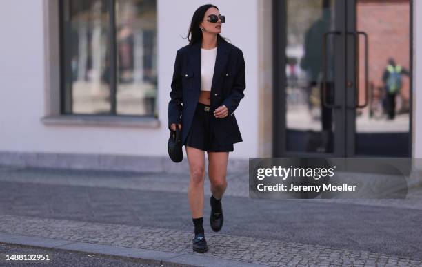 Anna Winter seen wearing Miu Miu black logo sunglasses, silver earrings, The Frankie Shop white cotton cropped top, Miu Miu navy blue blazer jacket,...