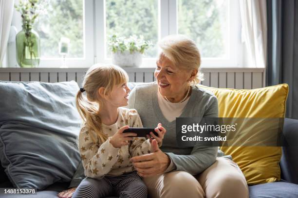 grand-mère et petit-enfant utilisant un téléphone intelligent - grandmas living room photos et images de collection