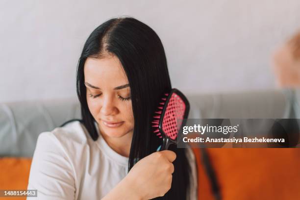 lady with black hair combing her hair while sitting on the couch - brushing hair stock pictures, royalty-free photos & images