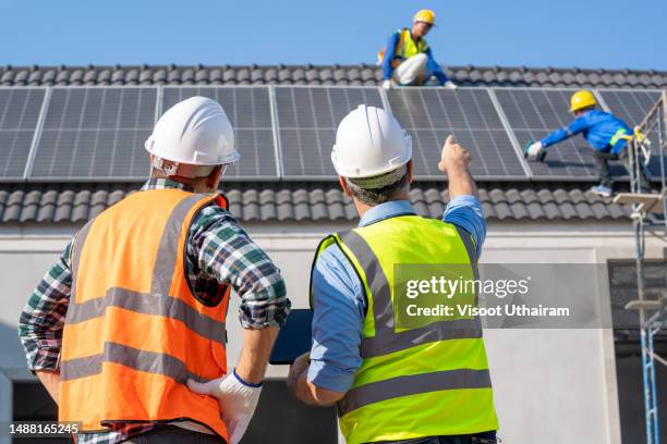 engineers in helmets installing solar panel system at roof top of home. - power occupation stock pictures, royalty-free photos & images