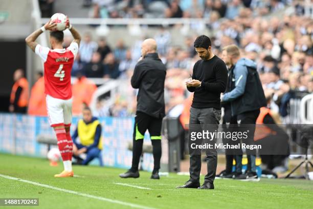 Mikel Arteta, Manager of Arsenal, makes notes as Ben White of Arsenal prepares to take a throw-in during the Premier League match between Newcastle...