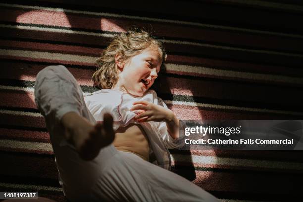 a young girl lies on a stripy carpet and laughs. she kicks her feet up in the air - tickling stock-fotos und bilder