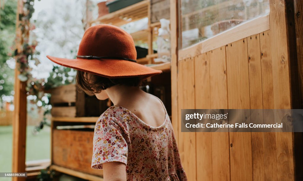 A little girl wearing a wide brim hat in a greenhouse