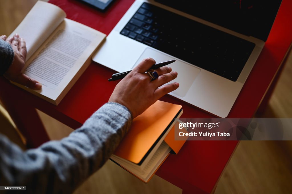 Woman's hand working with laptop and book.