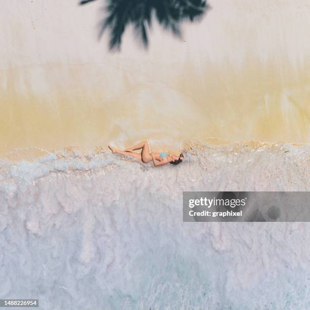 波しぶきのある砂浜に横たわる女性の空中ドローンビュー - 無人島 ストックフォトと画像