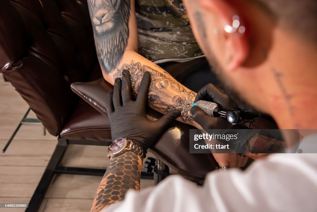 Close up of professional tattooer artist doing picture on hand of man by machine black ink from a jar. Tattoo art on body. Equipment for making tattoo art.