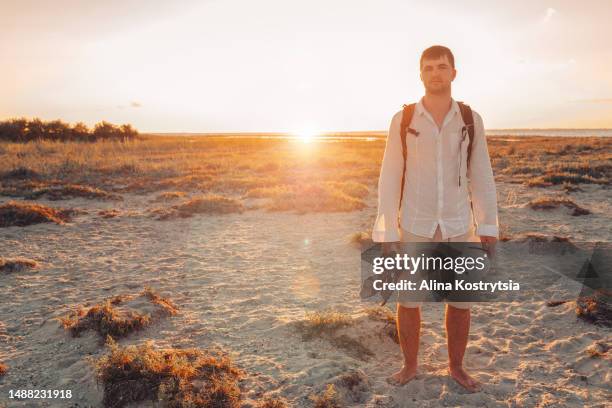 young handsome man stands barefoot on coast at bright sunset - beach top view stock-fotos und bilder