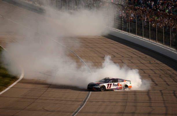 Denny Hamlin, driver of the FedEx Express Toyota, celebrates with a burnout after winning the NASCAR Cup Series Advent Health 400 at Kansas Speedway...