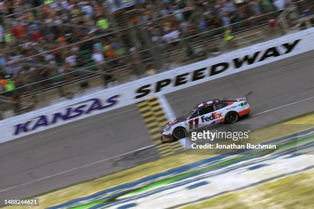 Denny Hamlin, driver of the FedEx Express Toyota, crosses the finish line to win the NASCAR Cup Series Advent Health 400 at Kansas Speedway on May...
