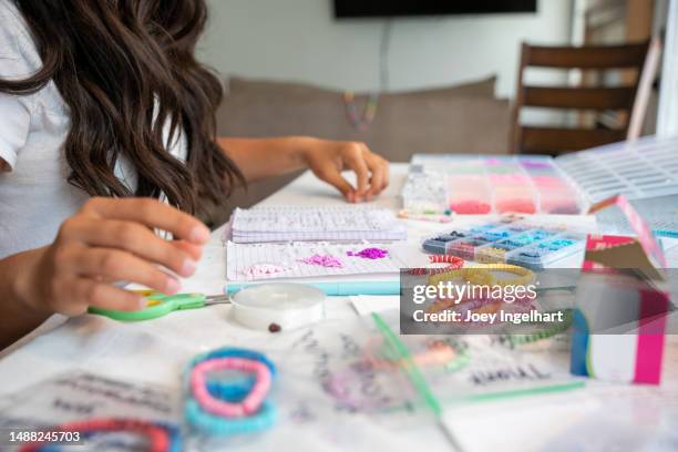 una niña de 12 a 14 años dentro de su casa está haciendo pulseras para vender para recaudar fondos - friendship-bracelet fotografías e imágenes de stock