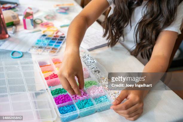 una niña de 12 a 14 años dentro de su casa está haciendo pulseras para vender para recaudar fondos - hacer cuentas fotografías e imágenes de stock