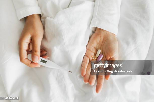 thermometer and medicine in female hands. daily antibiotic and antiviral pills. fever and cold - fish oil stock photos et images de collection