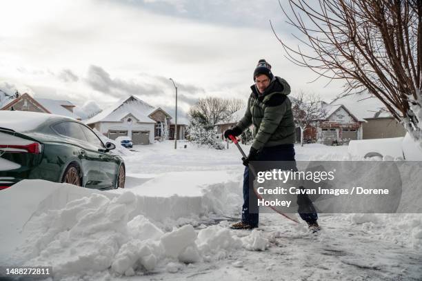 man shoveling snow off of his driveway after a winter storm - scavare foto e immagini stock