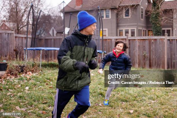 a happy boy chases father through yard in winter - columbus ohio winter stock pictures, royalty-free photos & images