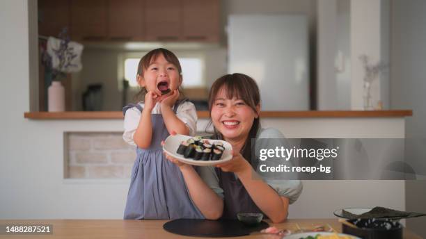 mother and daughter preparing and eating sushi at home - girl eating fish stock pictures, royalty-free photos & images