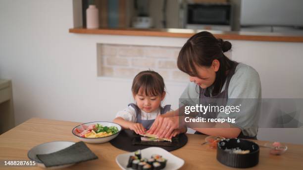 mother and daughter preparing and eating sushi at home - maki sushi stock pictures, royalty-free photos & images