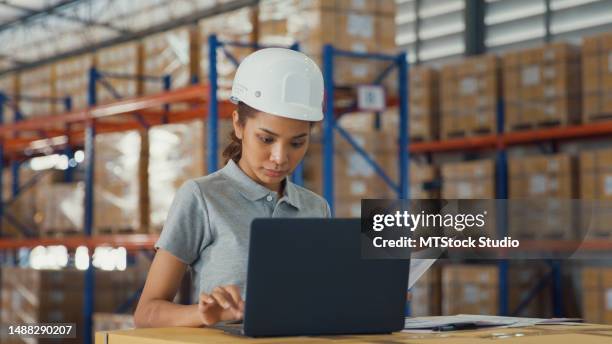 young asian woman warehouse worker checks stock and inventory with laptop in factory warehouse. logistic industry business. - transportation building type of building stock pictures, royalty-free photos & images