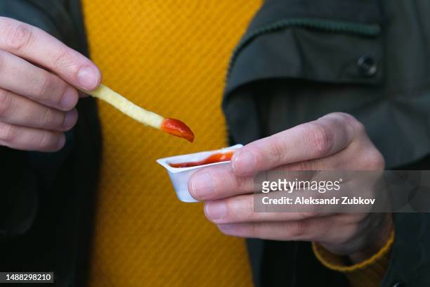 a man eats french fries with his hands, dips french fries in ketchup, dips it in sauce, in a cafe, restaurant, in a street or sidewalk cafe. american food, junk food and snacks. dependence on harmful unhealthy food. fast food. - georgian man stock pictures, royalty-free photos & images