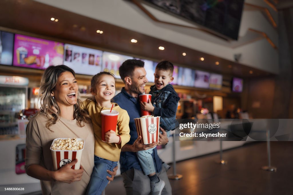 Young happy family with popcorn and drinks in movie theatre.