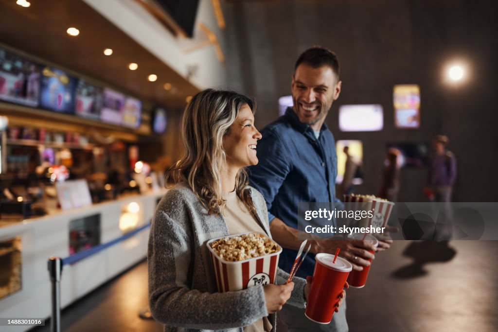 Happy couple bought popcorn and drinks before movie projection in cinema.