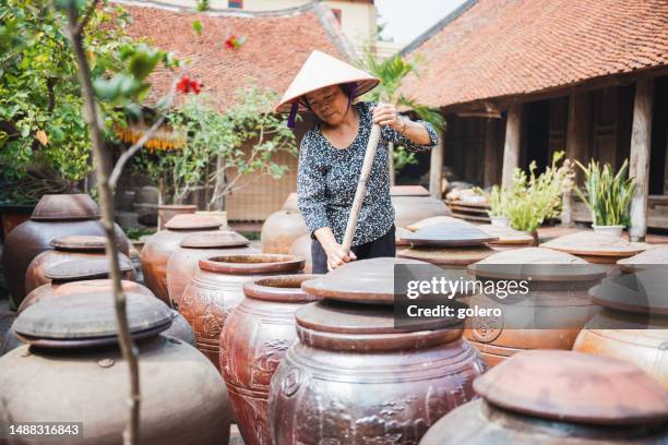 vietnamese senior woman stirring in huge clay soy pod in courtyard - vietnamese cuisine stock pictures, royalty-free photos & images
