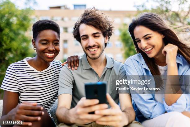 happy young group of millennial student people having fun together sharing social media content on cellphone network app. international friends enjoying time outdoors. - international student day stock-fotos und bilder