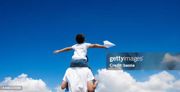 son sitting father's shoulder and throwing paper plane - fathers day stock pictures, royalty-free photos & images