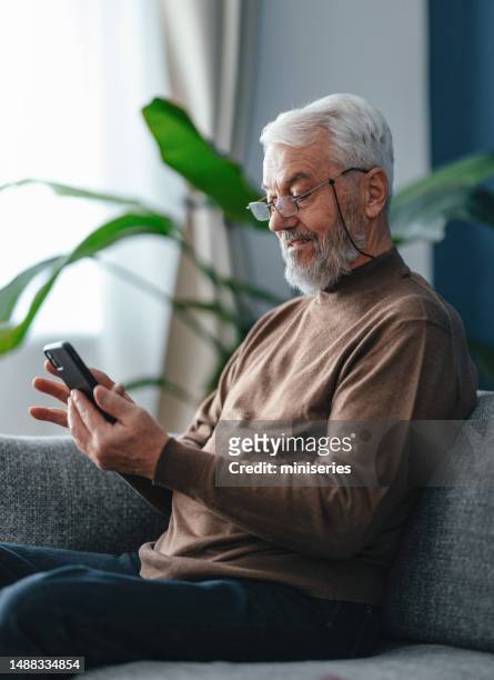 portrait of a senior man sitting at home and using his mobile phone - dial stock pictures, royalty-free photos & images
