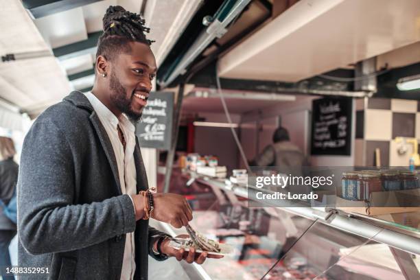 handsome diverse black man tourist in delft eating fish - market stall stock pictures, royalty-free photos & images