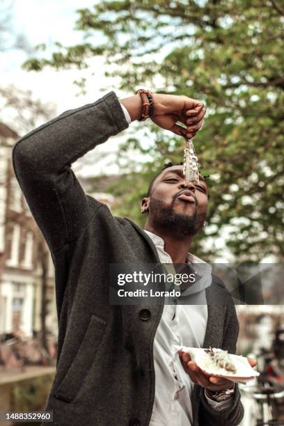 handsome diverse black man tourist in delft eating fish - herring bildbanksfoton och bilder