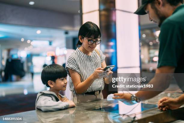 asian mother and son purchasing movie ticket at ticket counter  at movie theater cinema. - online payment stock pictures, royalty-free photos & images