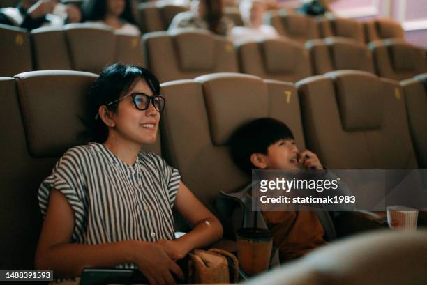 a beautiful mother takes her son to watch a movie at the cinema, and her son is very excited about watching this movie. - asian cinema stock pictures, royalty-free photos & images
