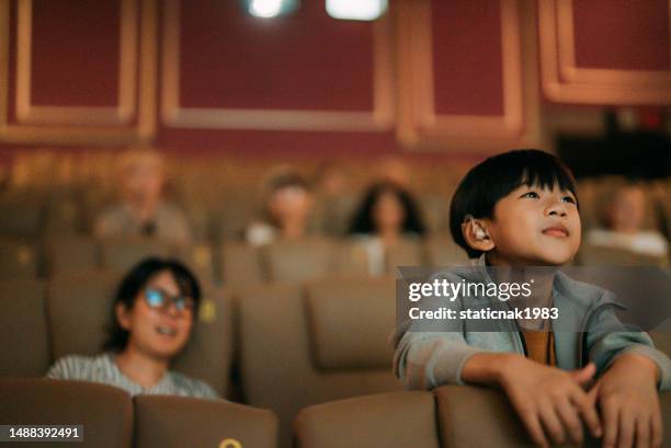 a boy intently watches a movie at the cinema, with his mother sitting behind him. - film screening stock pictures, royalty-free photos & images