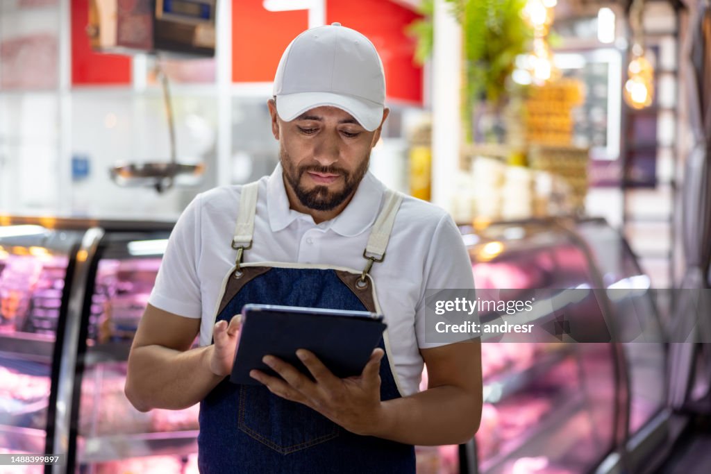 Man working at a butcherâs shop doing an inventory using a tablet