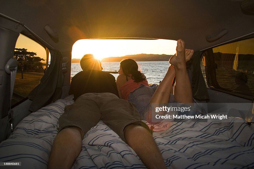 Couple watching sunset from bed inside campervan.