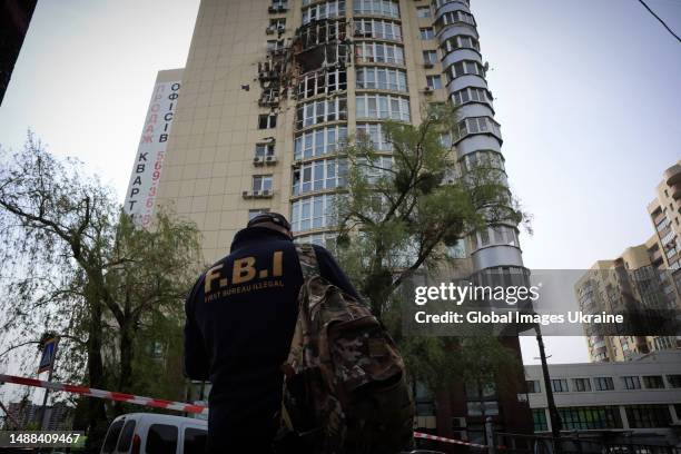 Man wearing a jacket with the inscription FBI stands near a high-rise residential building damaged by the downed Shahed kamikaze drone on May 8, 2023...