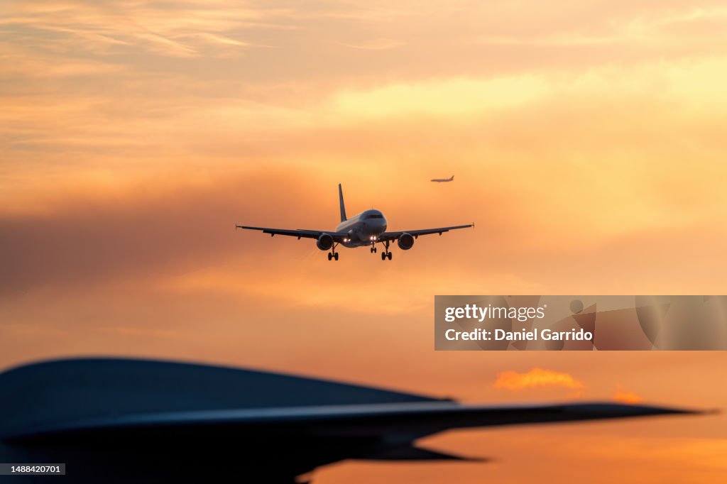 Sky high traffic, sunset arrival with blurred tail of parked plane and approaching jet