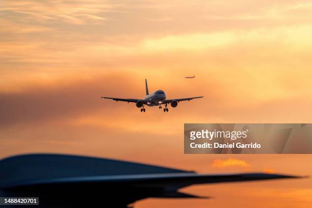sky high traffic, sunset arrival with blurred tail of parked plane and approaching jet - airplane tail - fotografias e filmes do acervo