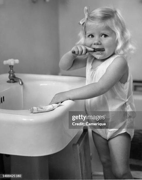 Little blond headed girl in her PJs standing on a stool next to the bathroom sink brushing her teeth