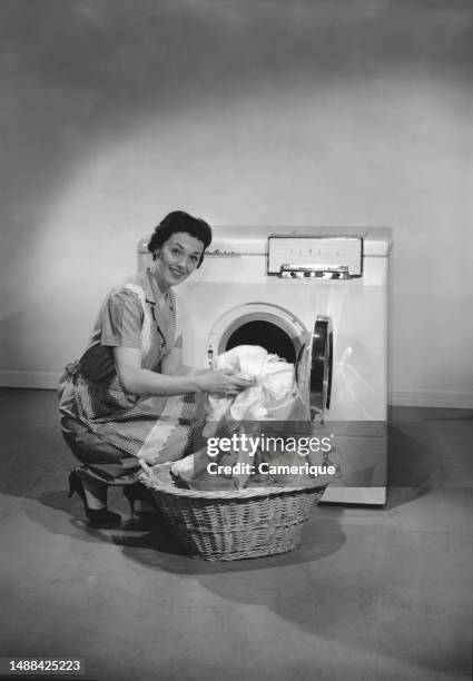 Young woman squatting down unloading a clothes dryer putting the clothes into a laundry basket.