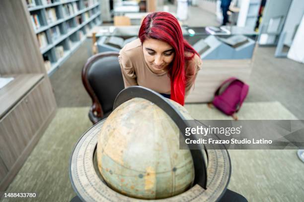 young woman looking at the world globe in the library at the university - world literature stock pictures, royalty-free photos & images